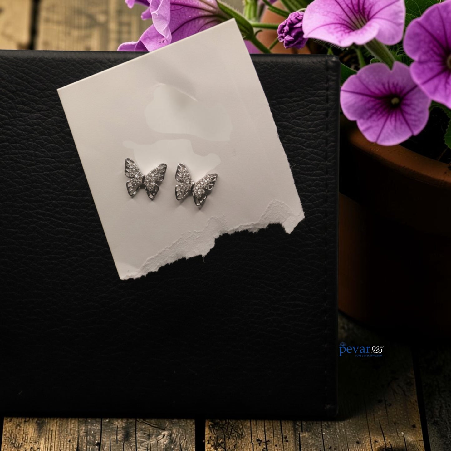 Butterfly-shaped earrings on a card with purple flowers in the background