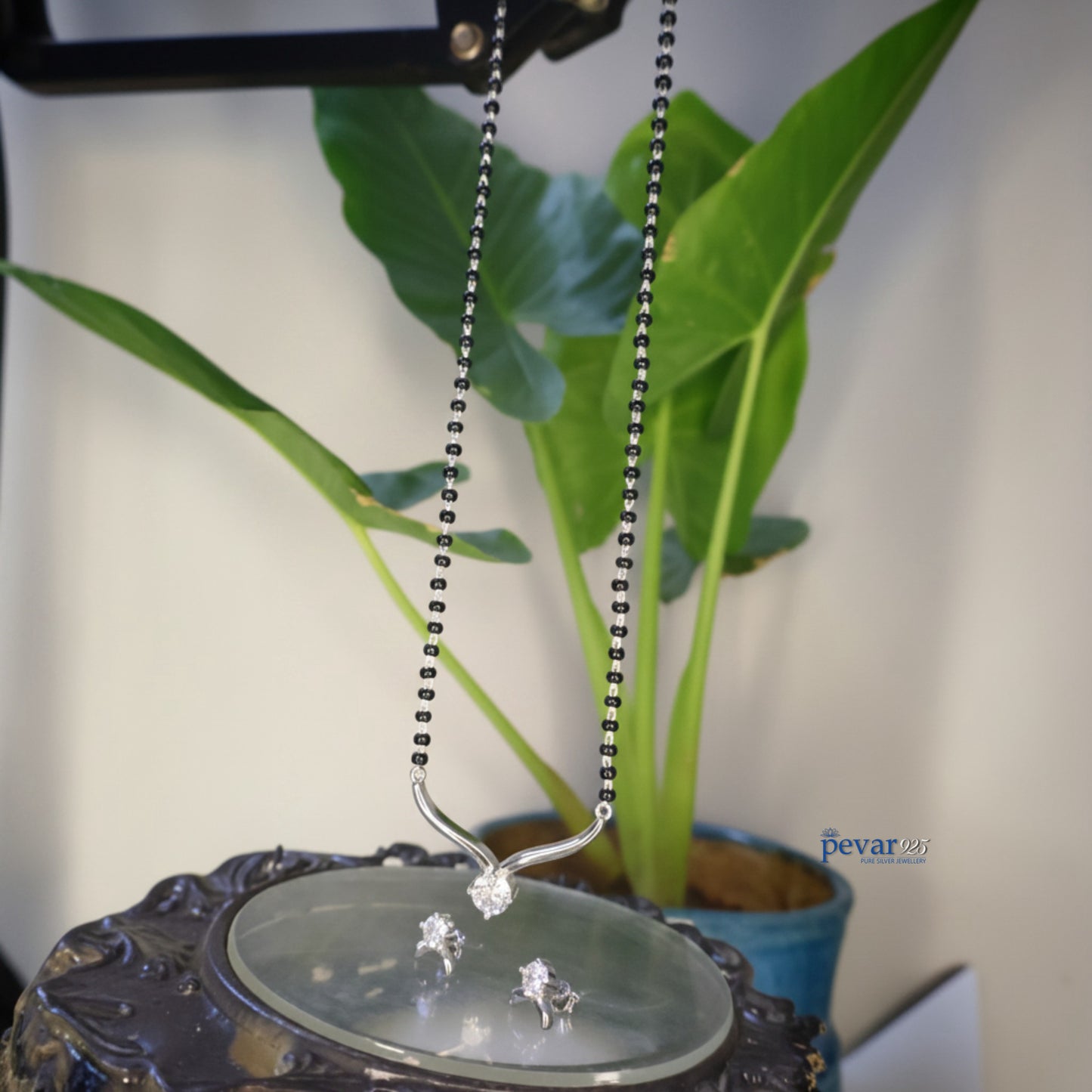 Silver necklace with a pendant on a decorative stand with a plant in the background