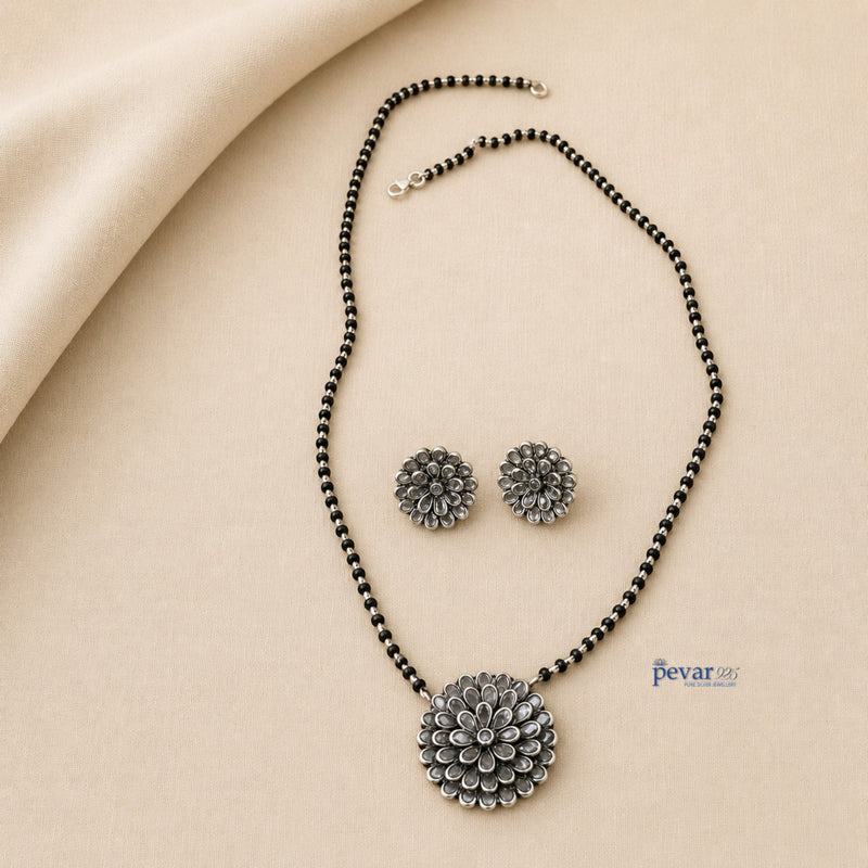 pevar925 oxidized silver mangalsutra set with floral glass charm pendant and matching stud earrings on beige fabric