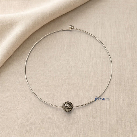 pevar925 oxidized silver hasli necklace with a central ornate bead featuring intricate swirl patterns on a beige fabric