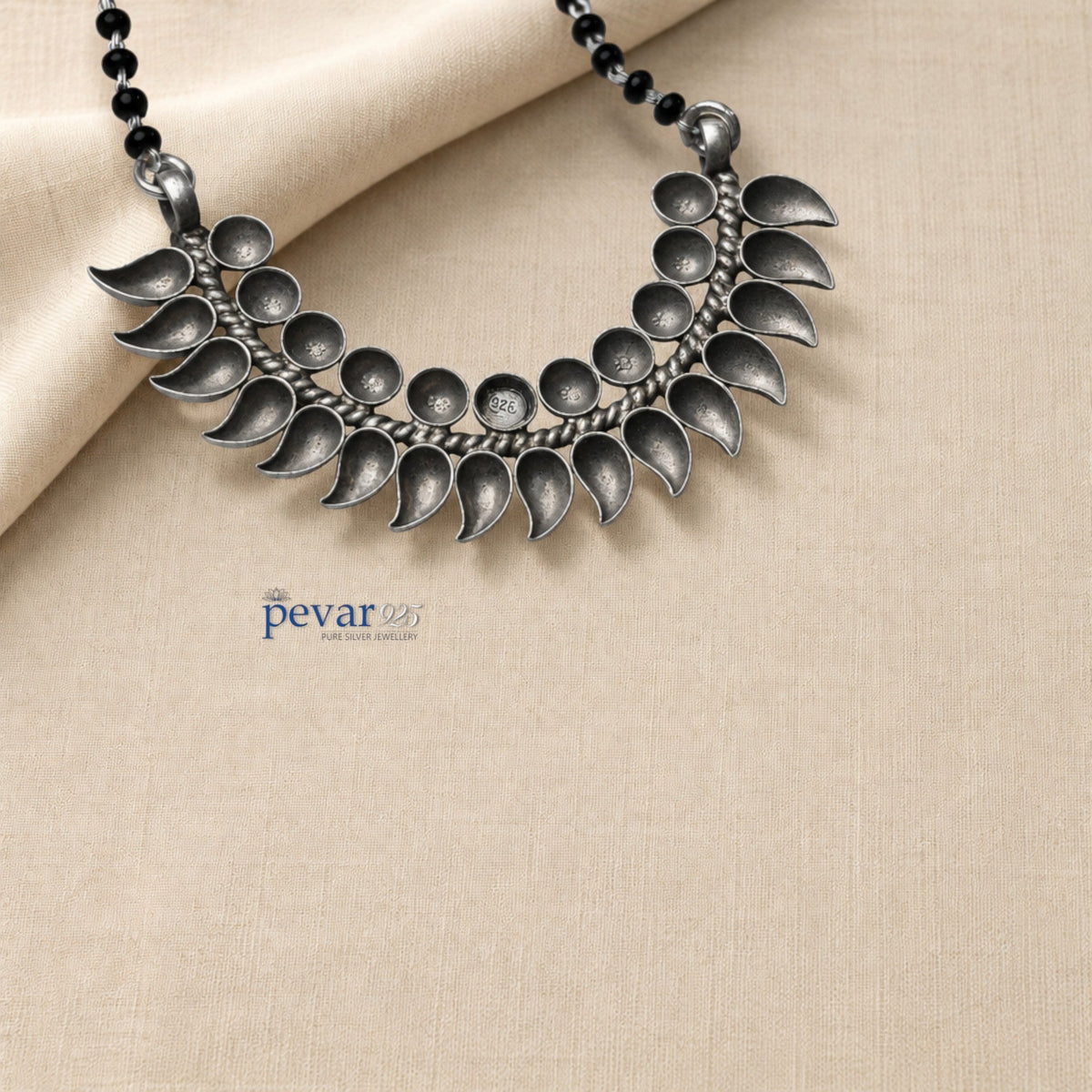 pevar925 oxidized 925 sterling silver mangalsutra with black beads and a crescent leaf motif pendant on beige fabric