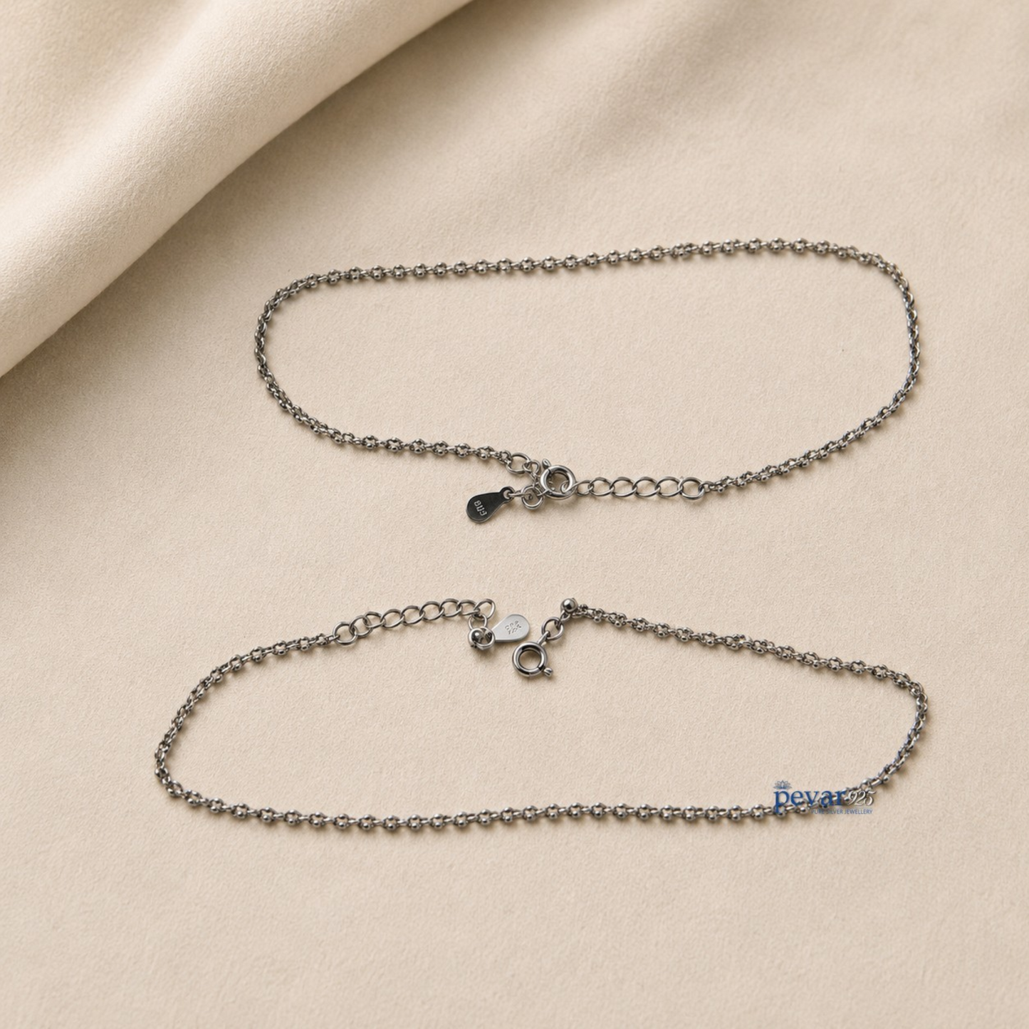 Two pevar925 sterling silver chain anklets with lobster clasps and adjustable extensions on a beige fabric background.