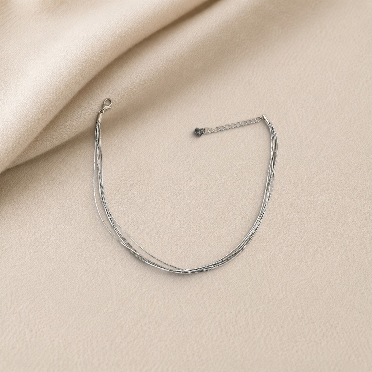 pevar925 sterling silver multi-strand anklet with a delicate heart-tag charm on a soft beige fabric background