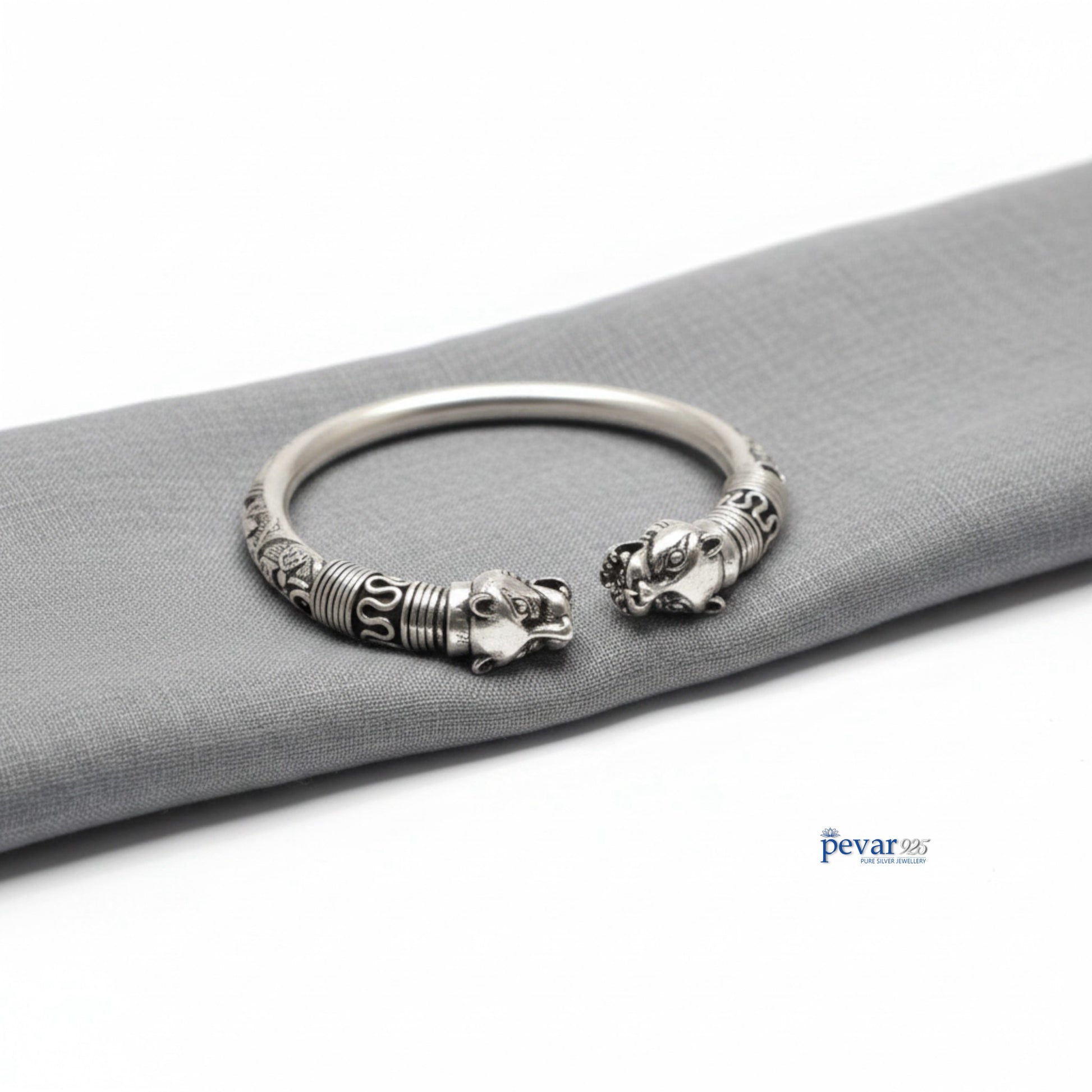 Silver bracelet with lion head designs on a gray surface