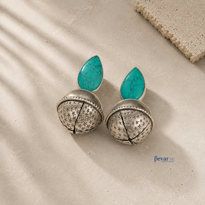Pair of silver earrings with turquoise leaves on a textured surface