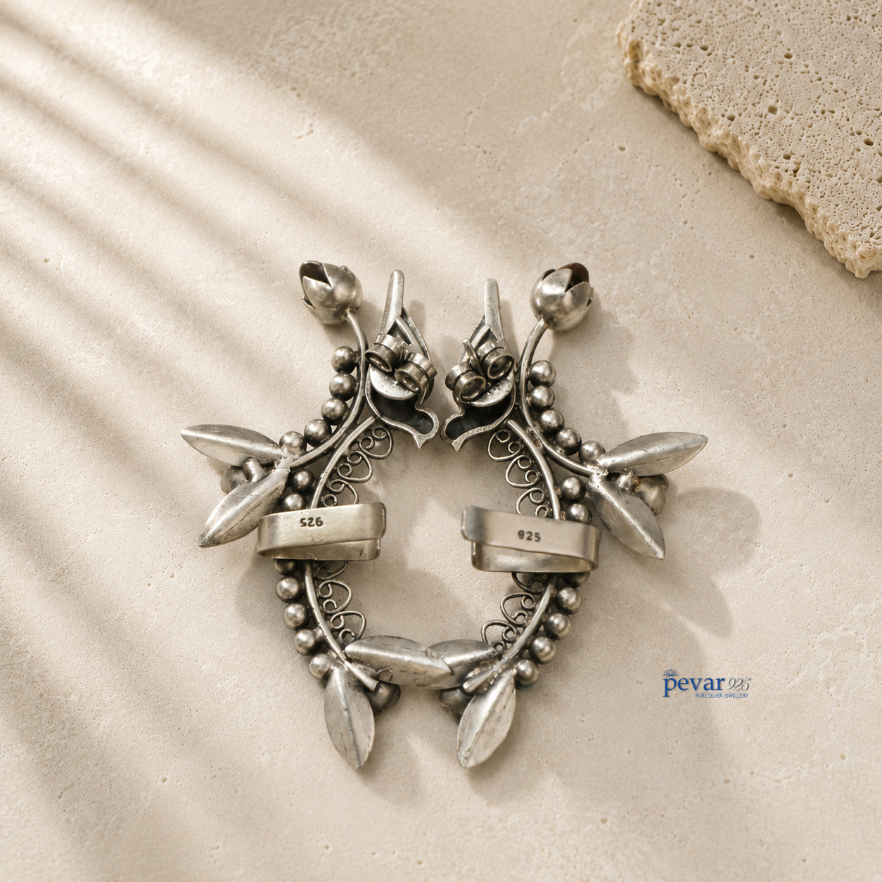 Silver Ear cuffs with leaf design on a textured beige surface