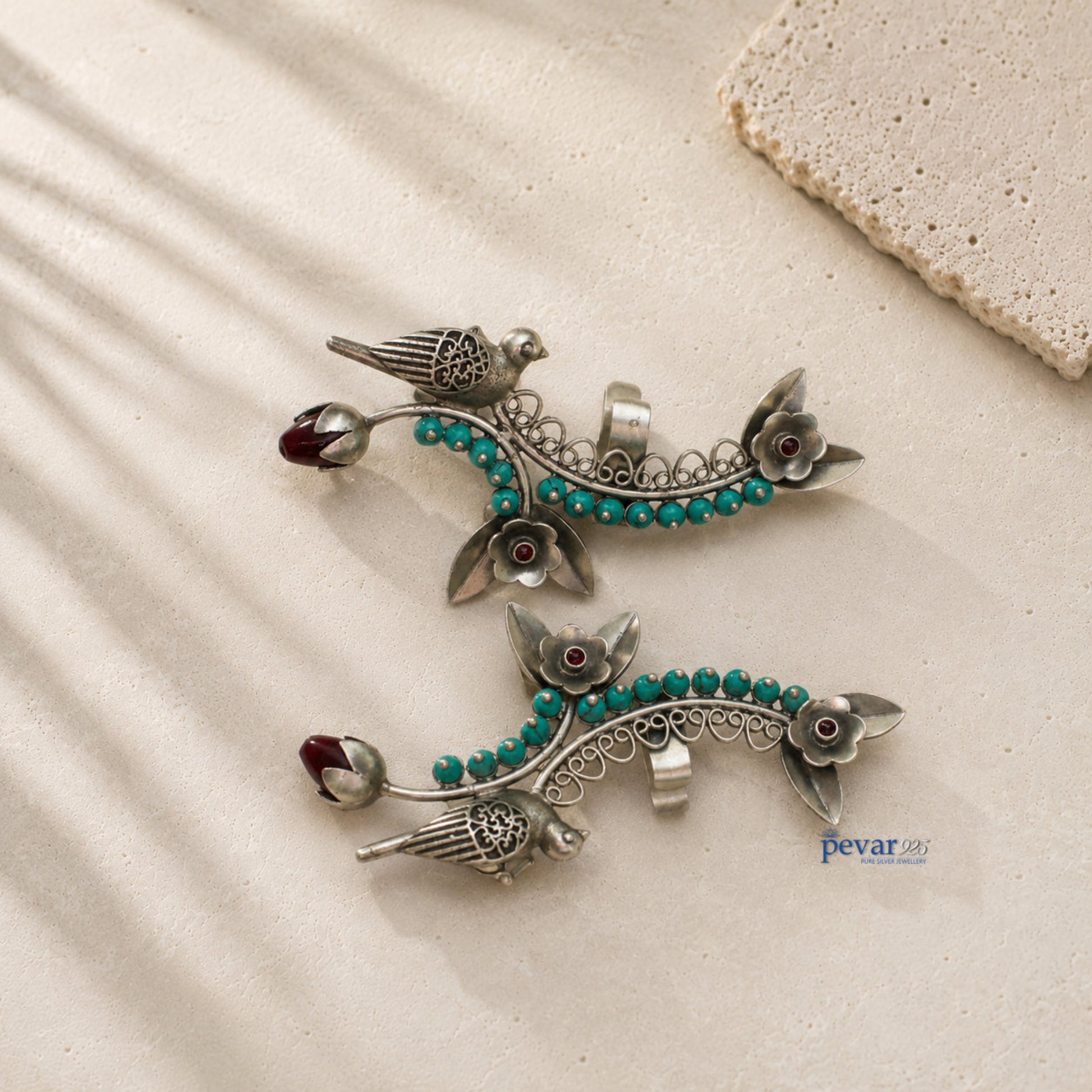 Pair of silver earrings with turquoise beads on a beige surface