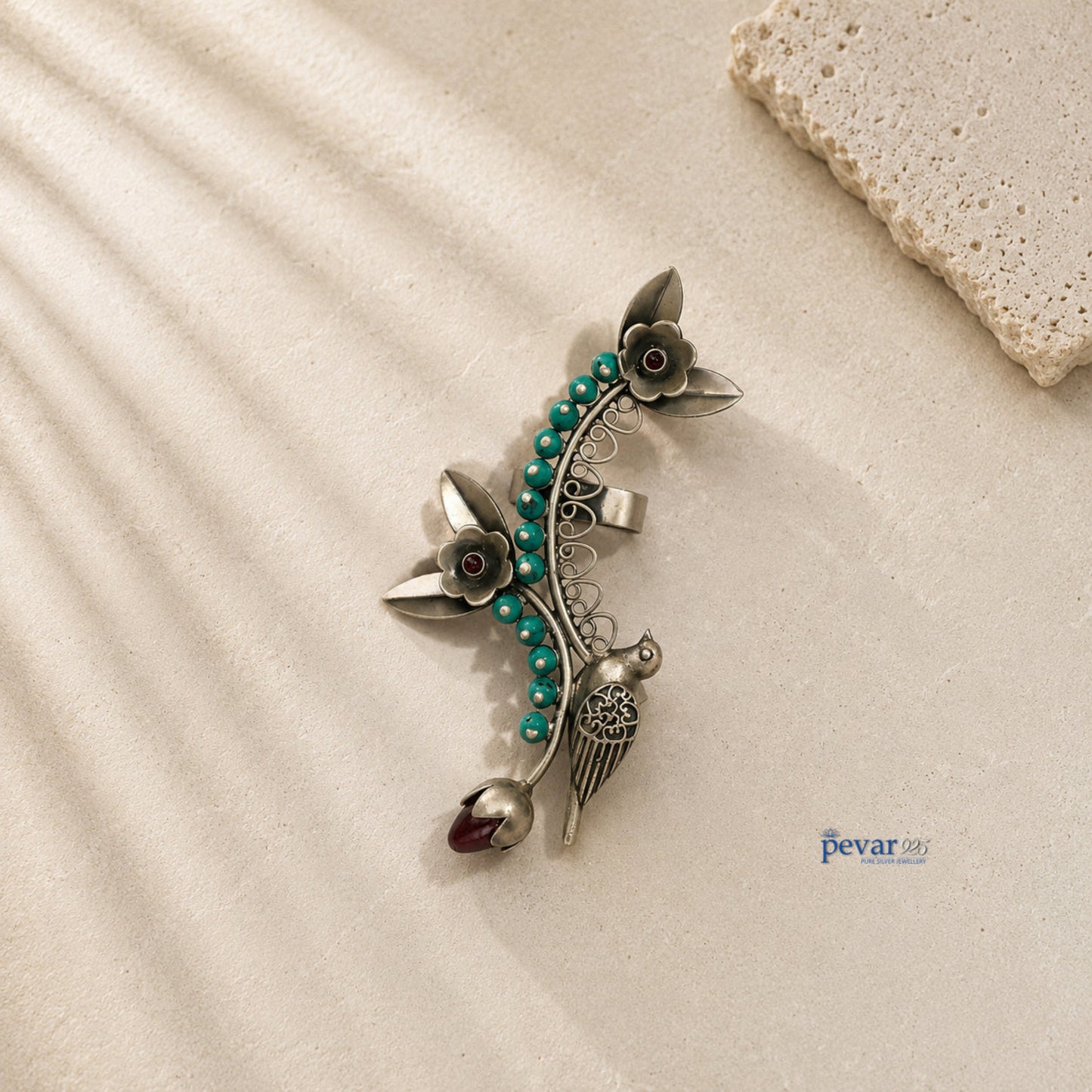 Decorative brooch with floral design and turquoise beads on a beige surface