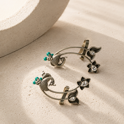 Silver earrings with floral designs and turquoise beads on a beige surface