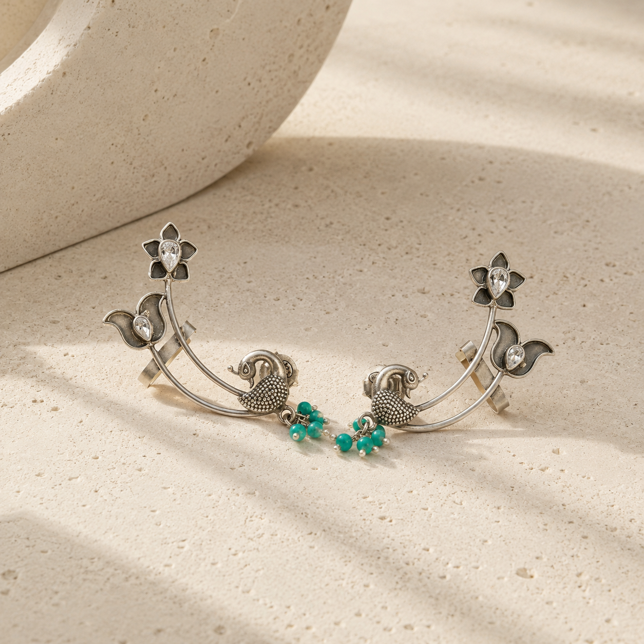Silver earrings with floral and bird designs on a beige surface