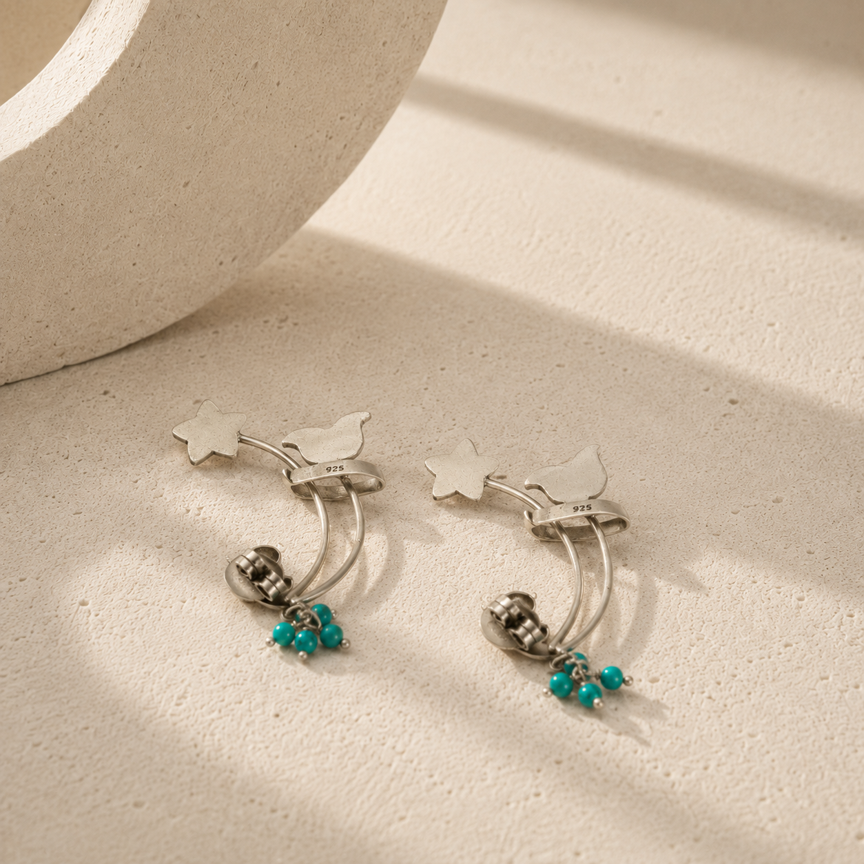 Silver earrings with turquoise beads on a textured beige surface
