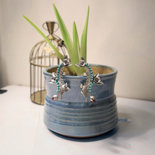 Pair of silver earrings with turquoise beads in a blue pot with a plant