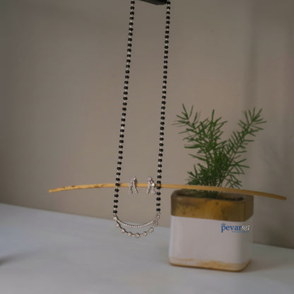Necklace with chain detail on a stick next to a plant in a pot with 'pevar' branding.