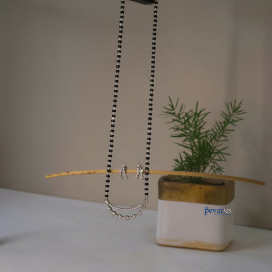 Necklace with chain detail on a stick next to a plant in a pot with 'pevar' branding.