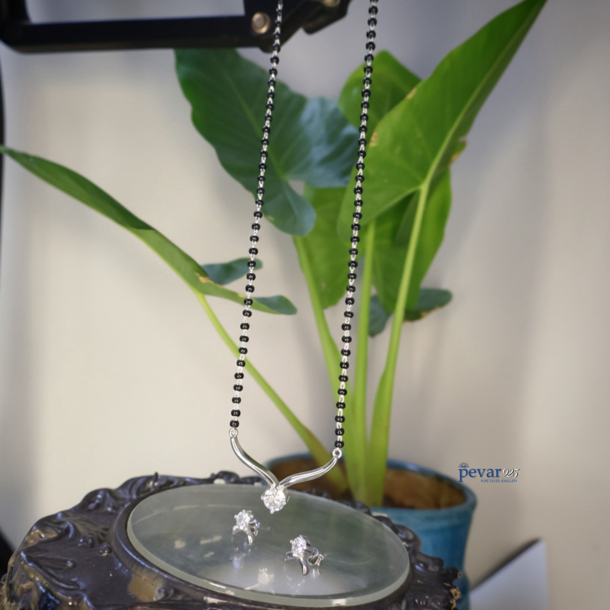 Silver necklace with a pendant on a decorative stand with a plant in the background