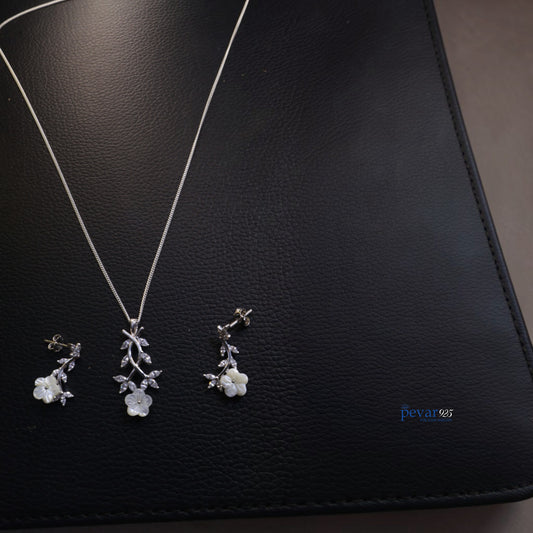 Silver floral necklace and earrings on a black leather surface with 'pevar' branding.