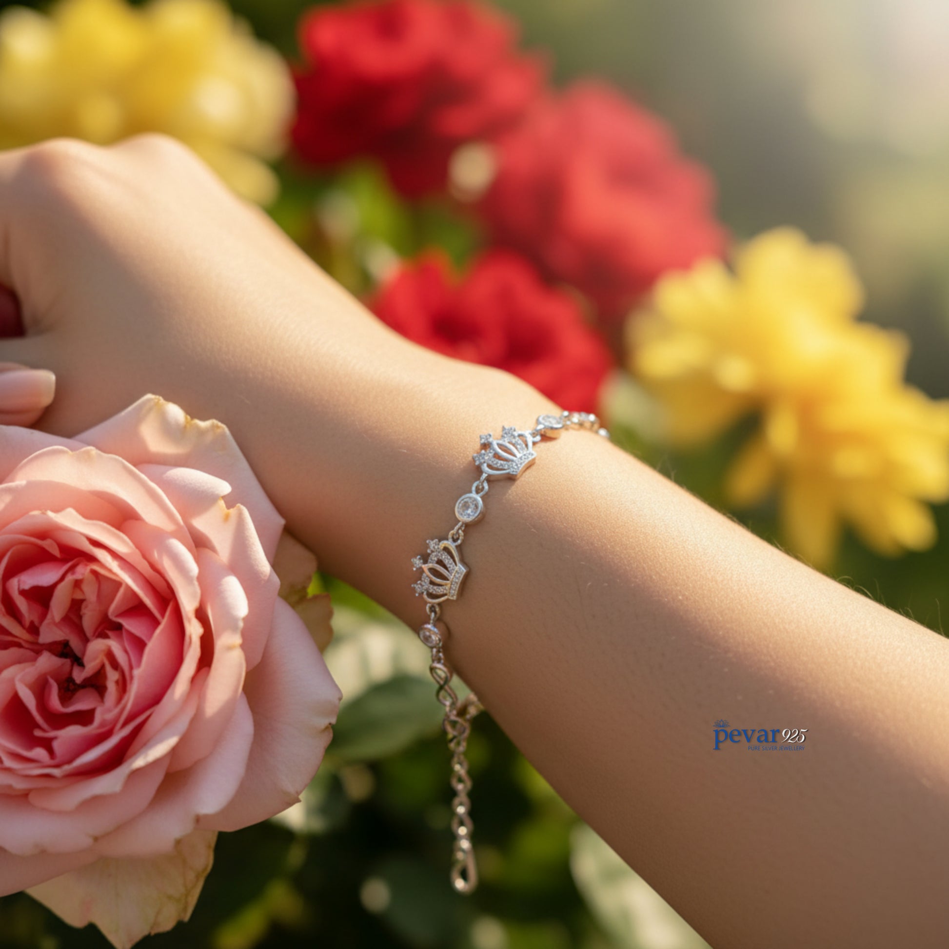 Hand wearing a silver bracelet holding a pink rose with blurred flowers in the background