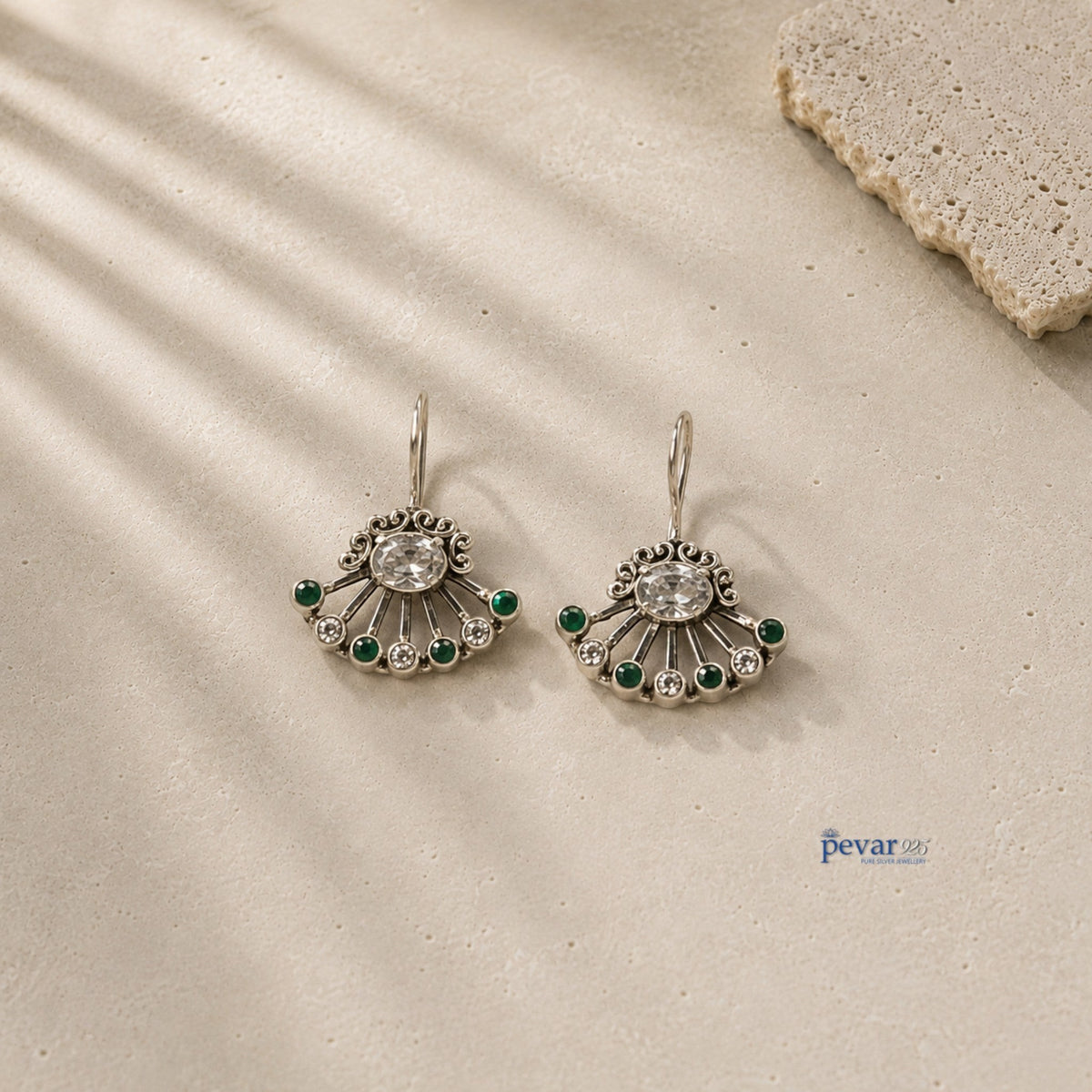 pevar925 oxidized 925 silver fan earrings with green stones and clear crystals on a textured stone surface