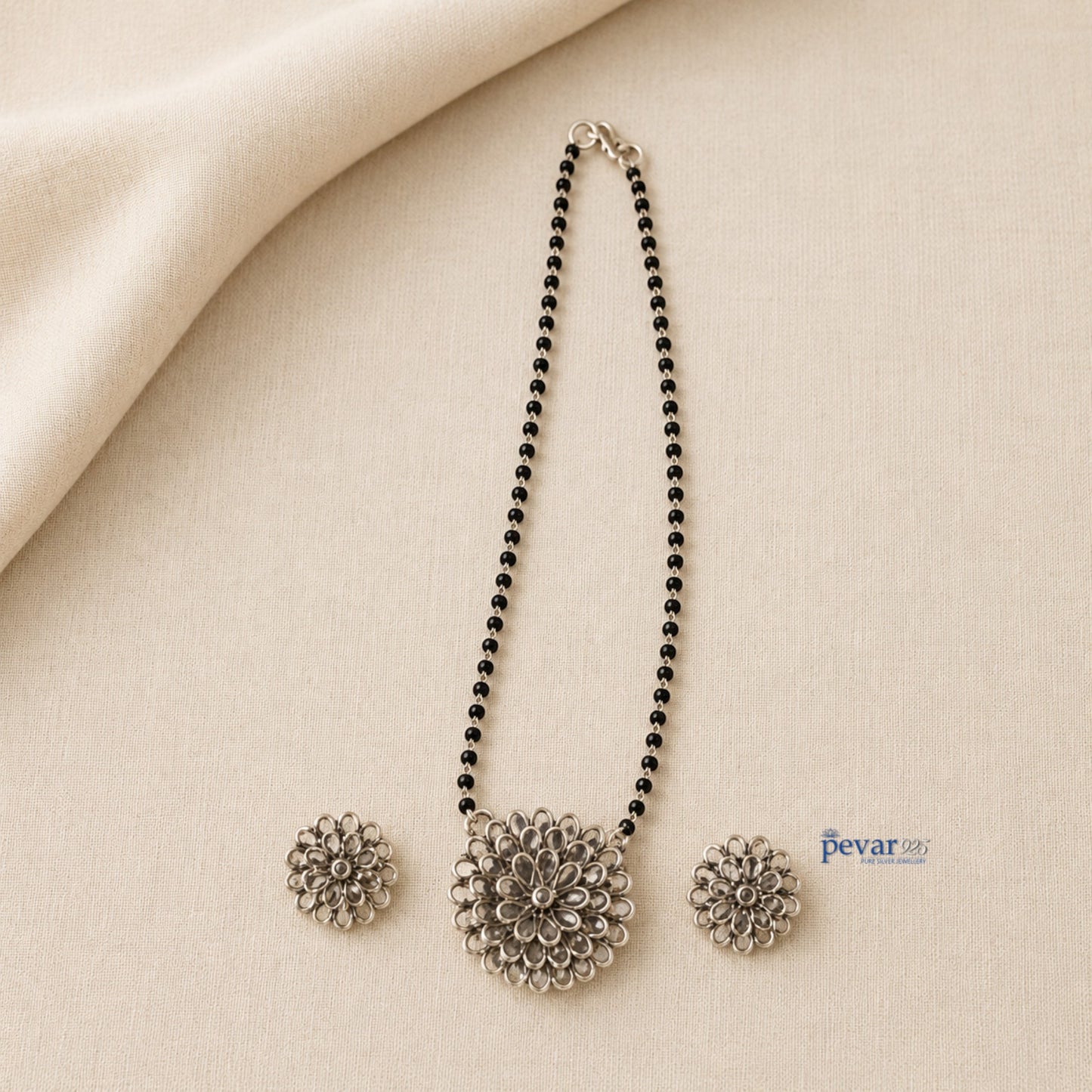 pevar925 oxidized silver mangalsutra set with floral glass charm pendant and matching earrings on beige fabric