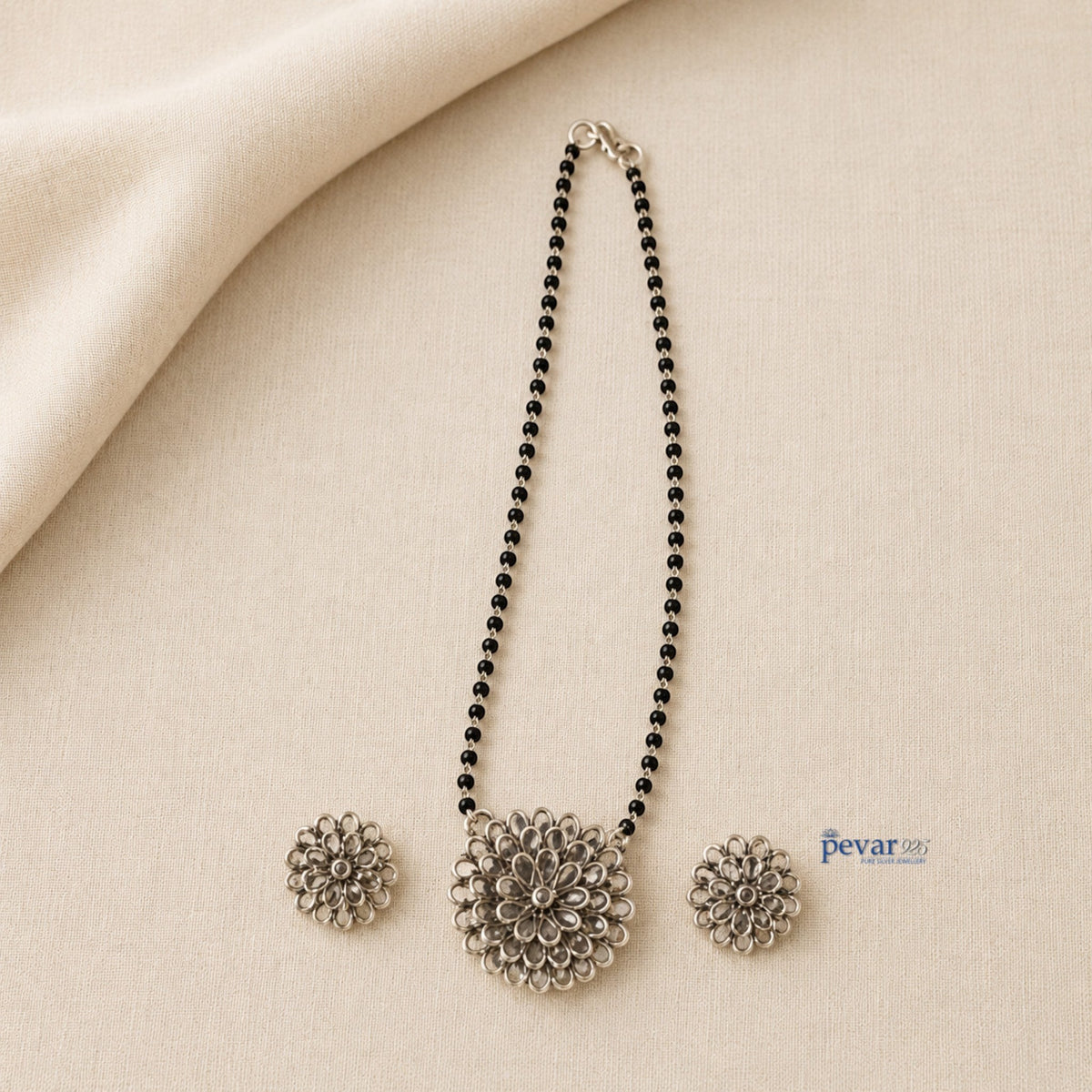 pevar925 oxidized silver mangalsutra set with floral glass charm pendant and matching earrings on beige fabric