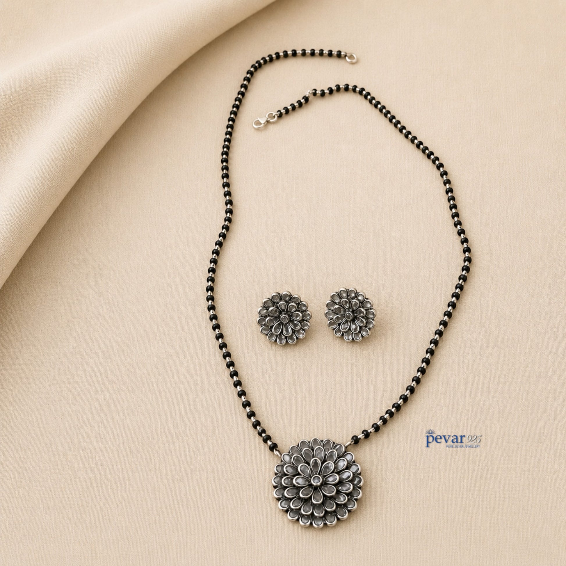pevar925 oxidized silver mangalsutra set with floral glass charm pendant and matching stud earrings on beige fabric