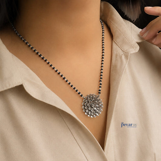pevar925 oxidized silver mangalsutra with a floral glass pendant and black beads worn on a beige shirt