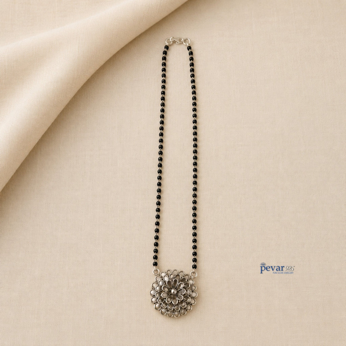 pevar925 oxidized silver mangalsutra with a floral glass pendant and black beads on a neutral fabric background.