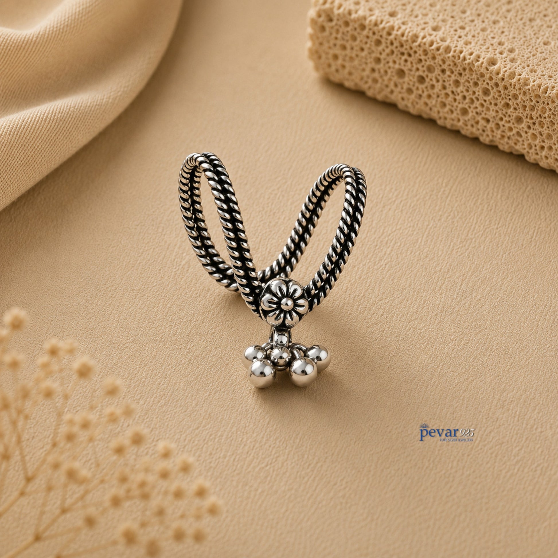 pevar925 oxidized silver V-shape ring with floral motif and dangling ghunghroo beads on a beige textured background.