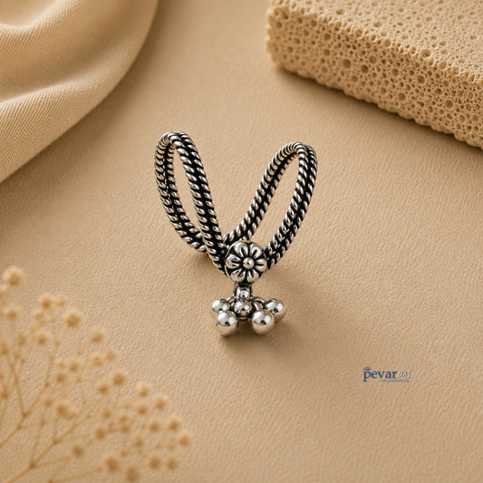 pevar925 oxidized silver V-shape ring with floral motif and dangling ghunghroo beads on a beige textured background.