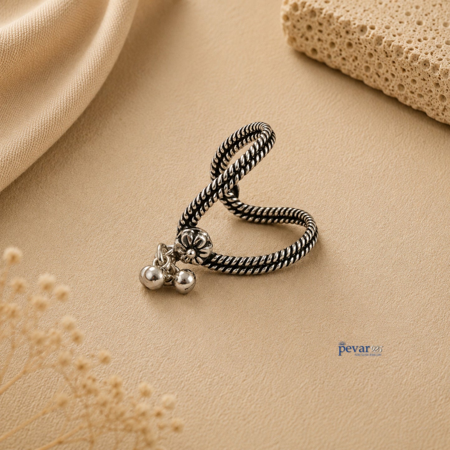 pevar925 oxidized silver V-shaped ring with floral motif and dangling ghunghroo beads on a textured beige background