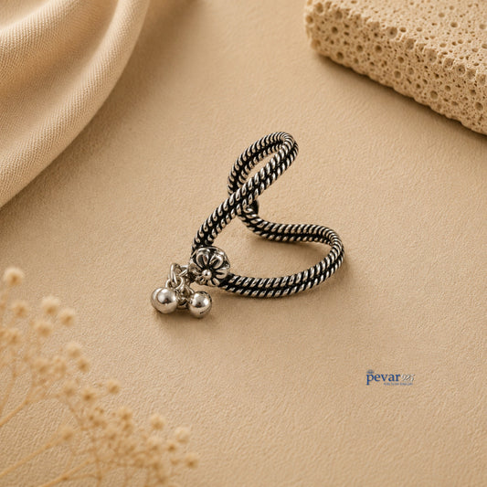 pevar925 oxidized silver V-shaped ring with floral motif and dangling ghunghroo beads on a textured beige background