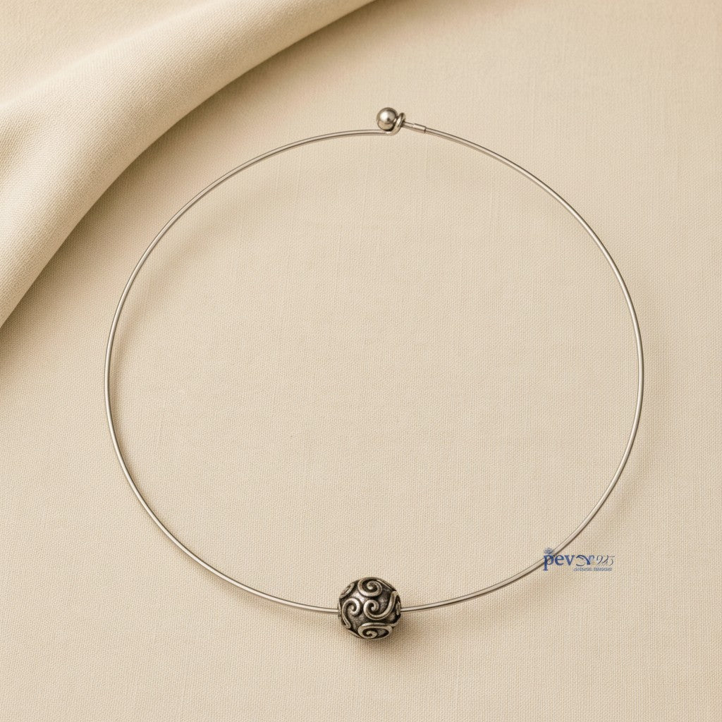 pevar925 oxidized silver hasli necklace with a central ornate bead featuring intricate swirl patterns on a beige fabric
