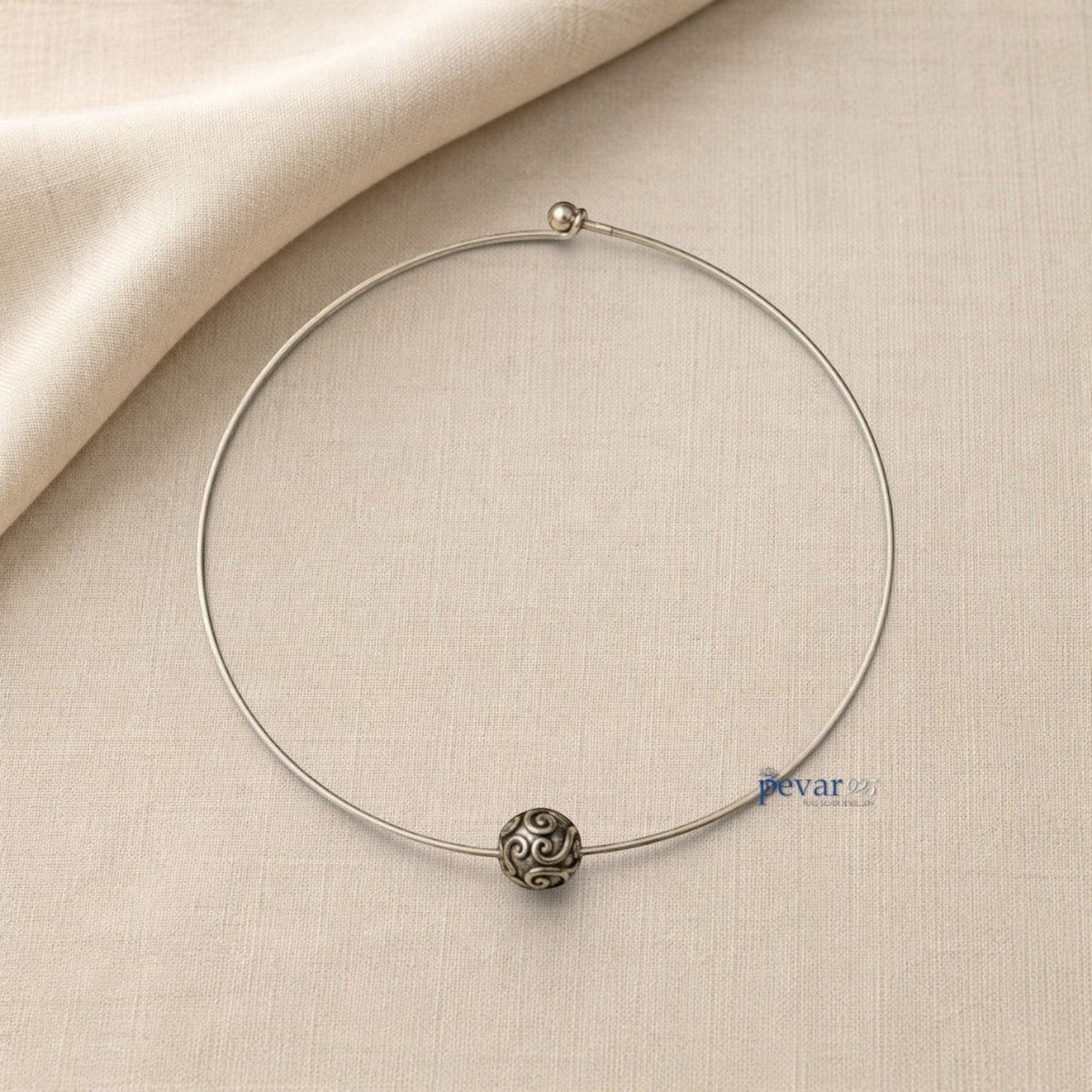 pevar925 oxidized silver hasli necklace with a central ornate bead featuring intricate swirl patterns on a beige fabric