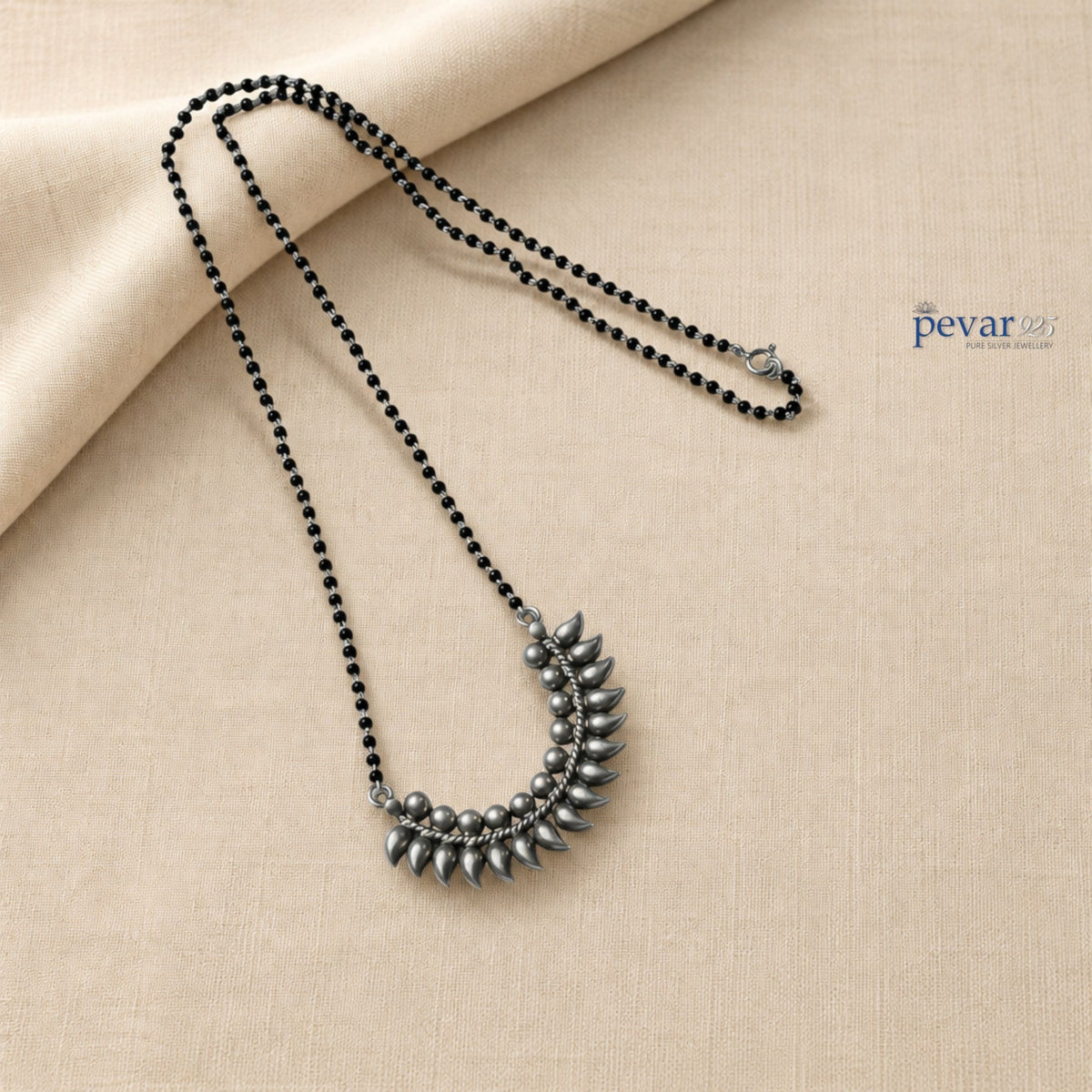 pevar925 oxidized sterling silver mangalsutra with black beads and a crescent leaf motif pendant on beige fabric