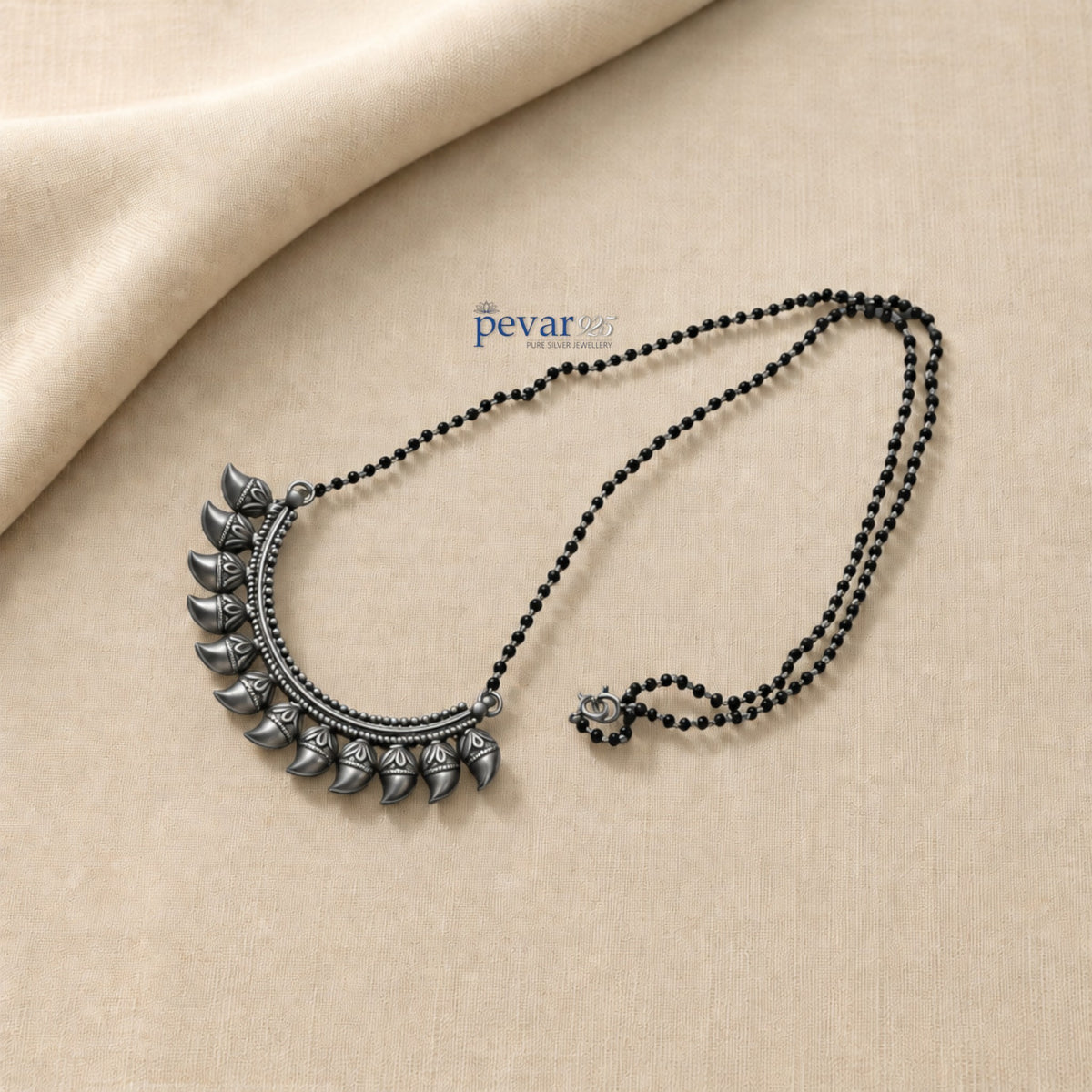 pevar925 oxidized 925 sterling silver mangalsutra with black beads and a crescent leaf motif pendant on beige fabric