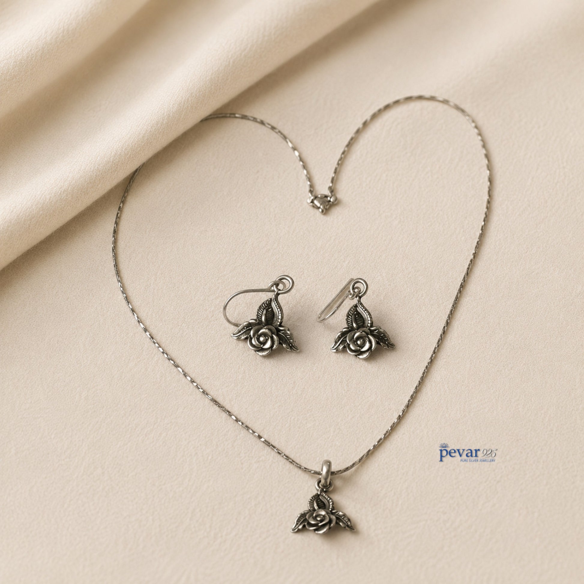 pevar925 oxidized silver rose petal pendant necklace and matching hook earrings on a soft beige fabric background