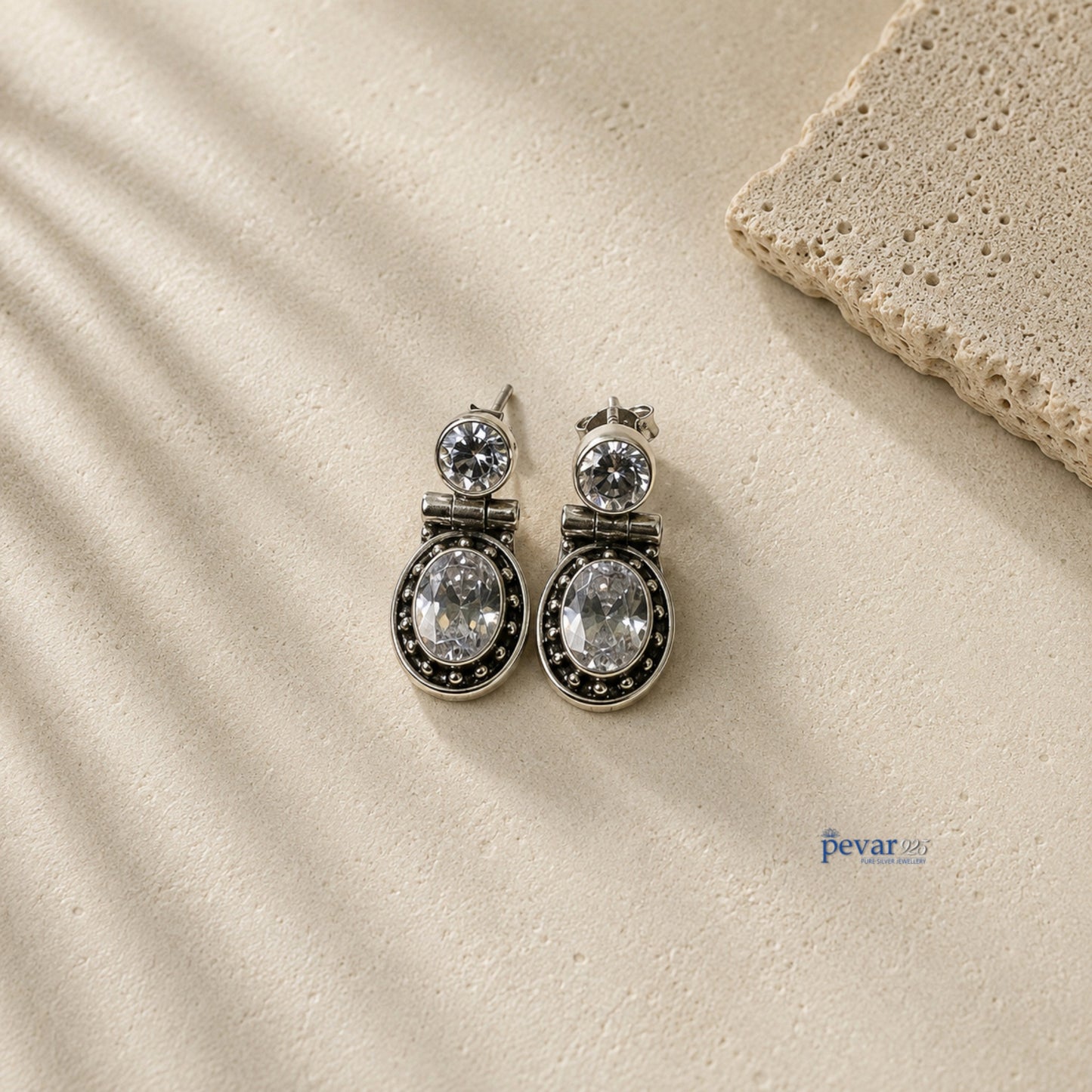pevar925 oxidized 925 silver hook earrings featuring sparkling oval stones on a textured stone surface.