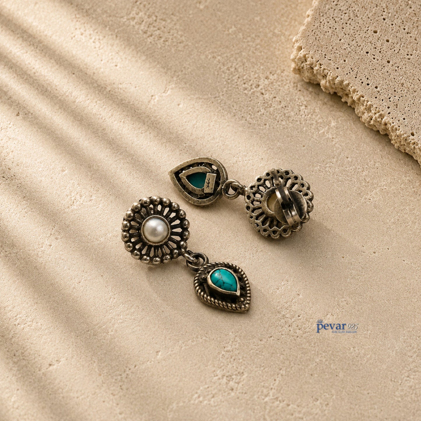 pevar925 oxidized 925 silver earrings featuring a round pearl and a teardrop turquoise stone on a textured beige surface.