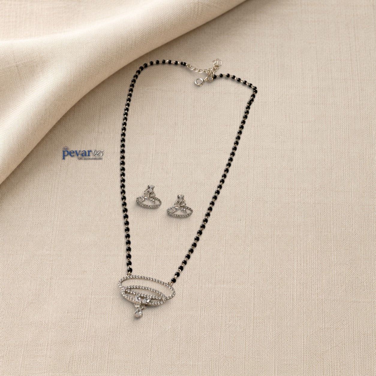 pevar925 sterling silver mangalsutra set with dual oval stone pendant, black beads, and matching earrings on fabric.