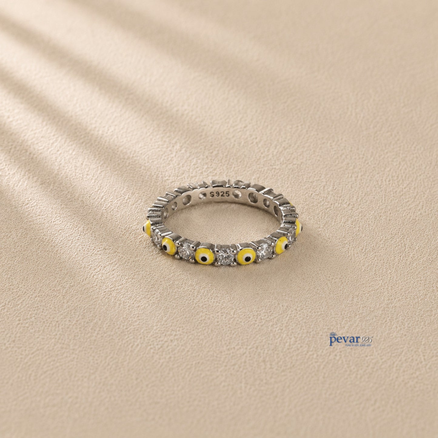 pevar925 sterling silver band ring featuring alternating yellow evil eye motifs and clear stones on a beige surface