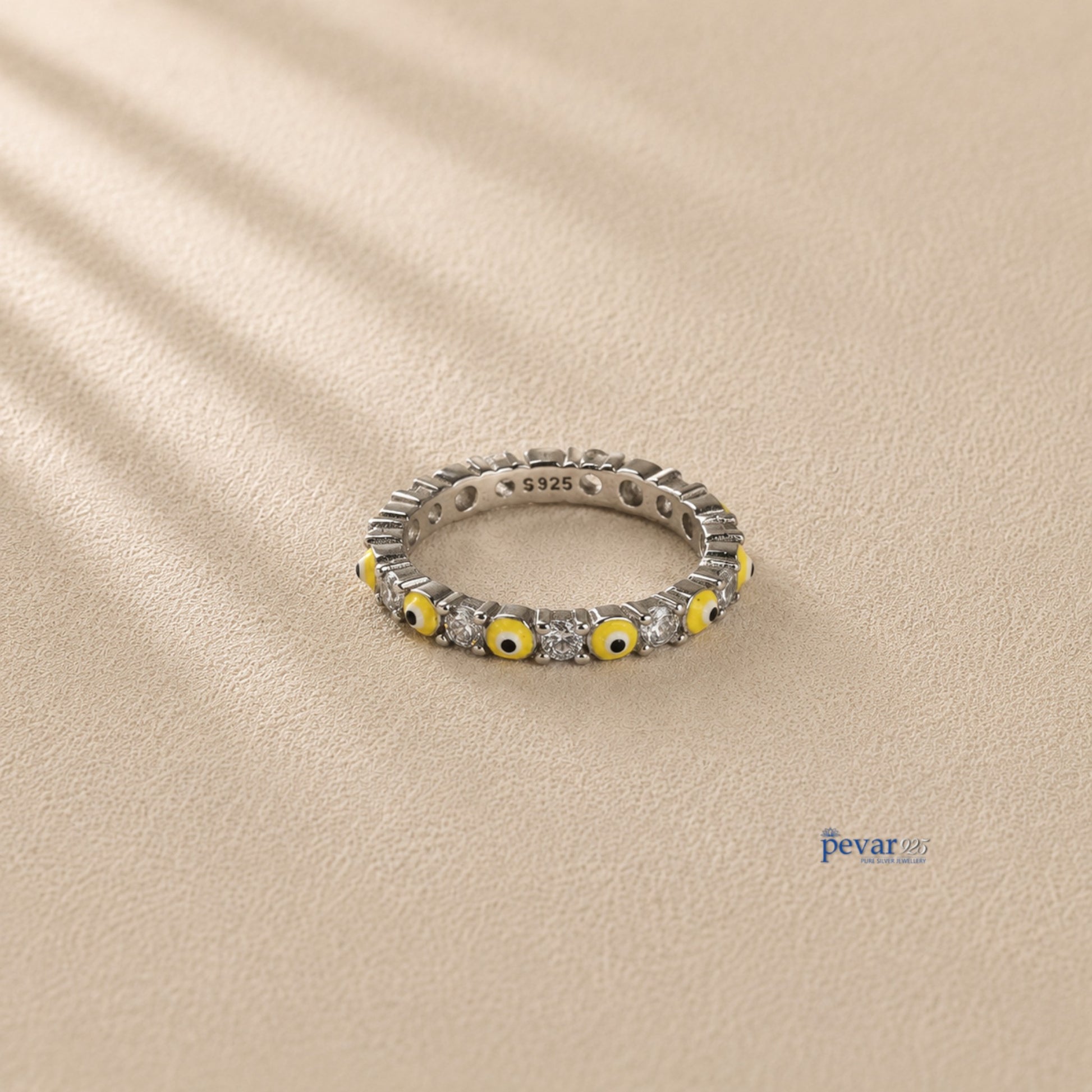 pevar925 sterling silver band ring featuring alternating yellow evil eye motifs and clear stones on a beige surface