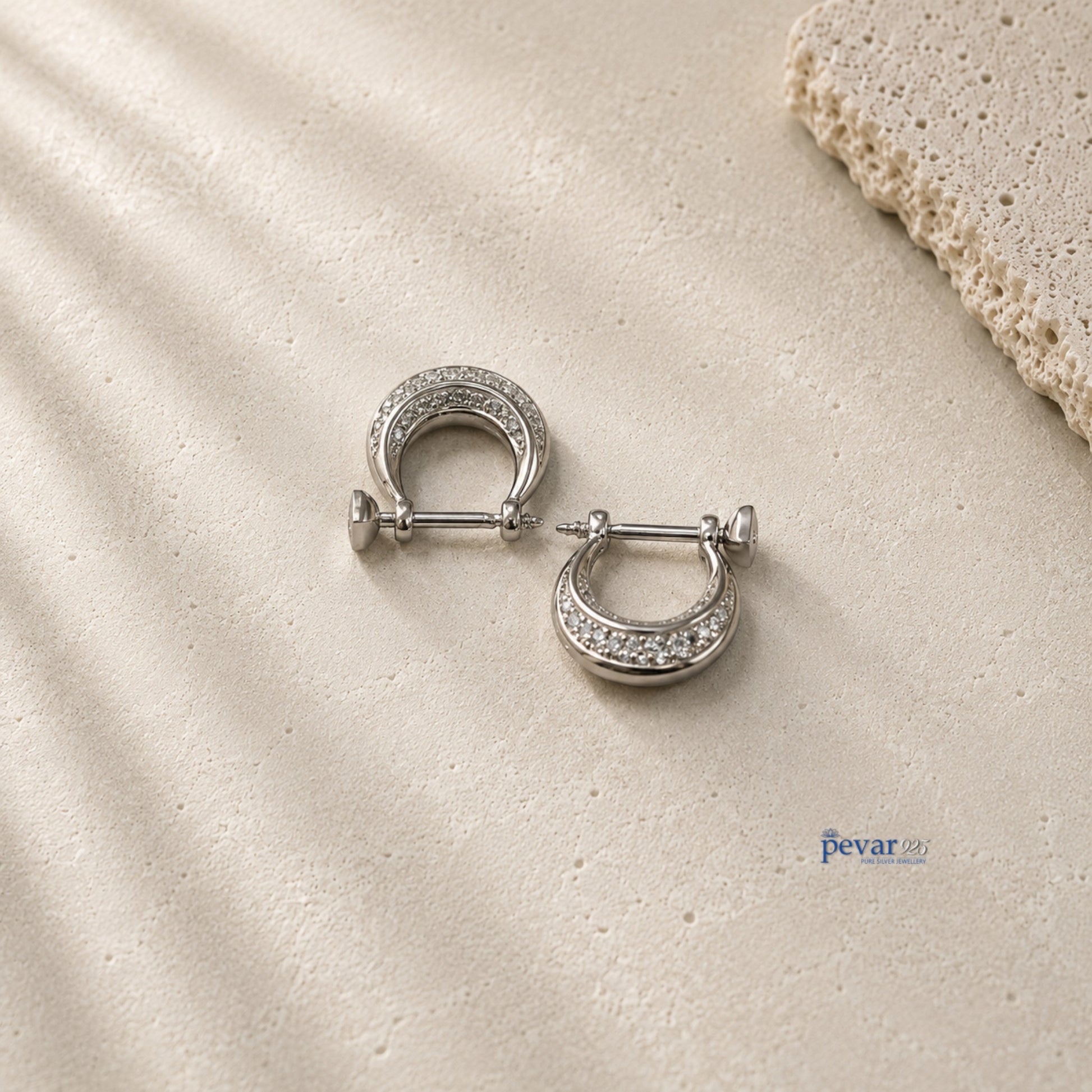 pevar925 sterling silver hoop earrings with rhodium plating and sparkling stones on a textured beige surface