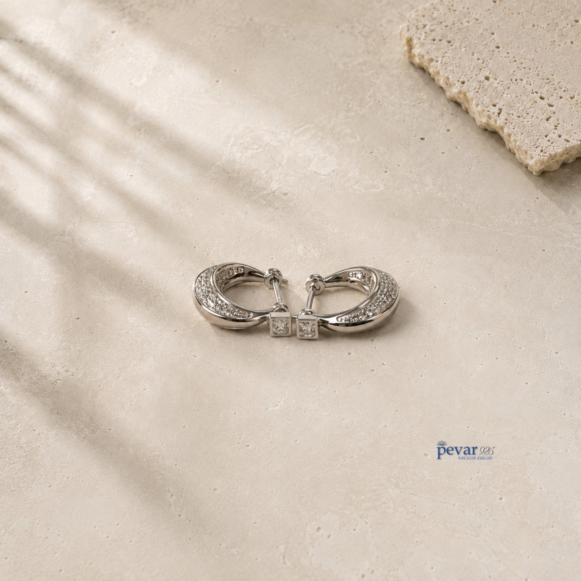 pevar925 sterling silver hoop earrings with rhodium plating and sparkling accents on a textured stone surface