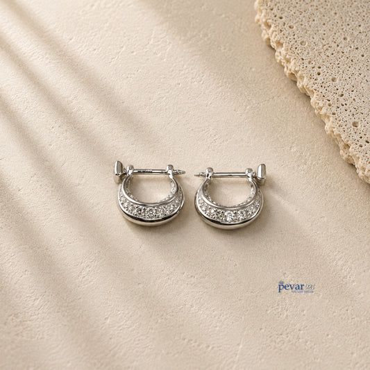 pevar925 sterling silver hoop earrings with rhodium plating and sparkling stones on a textured beige surface