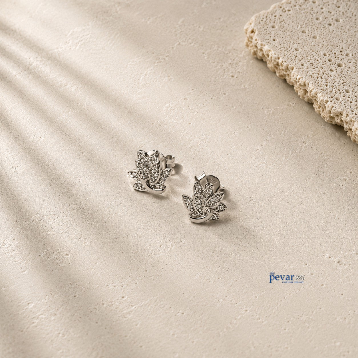 pevar925 sterling silver lotus stud earrings with rhodium plating and intricate detailing on a textured beige surface