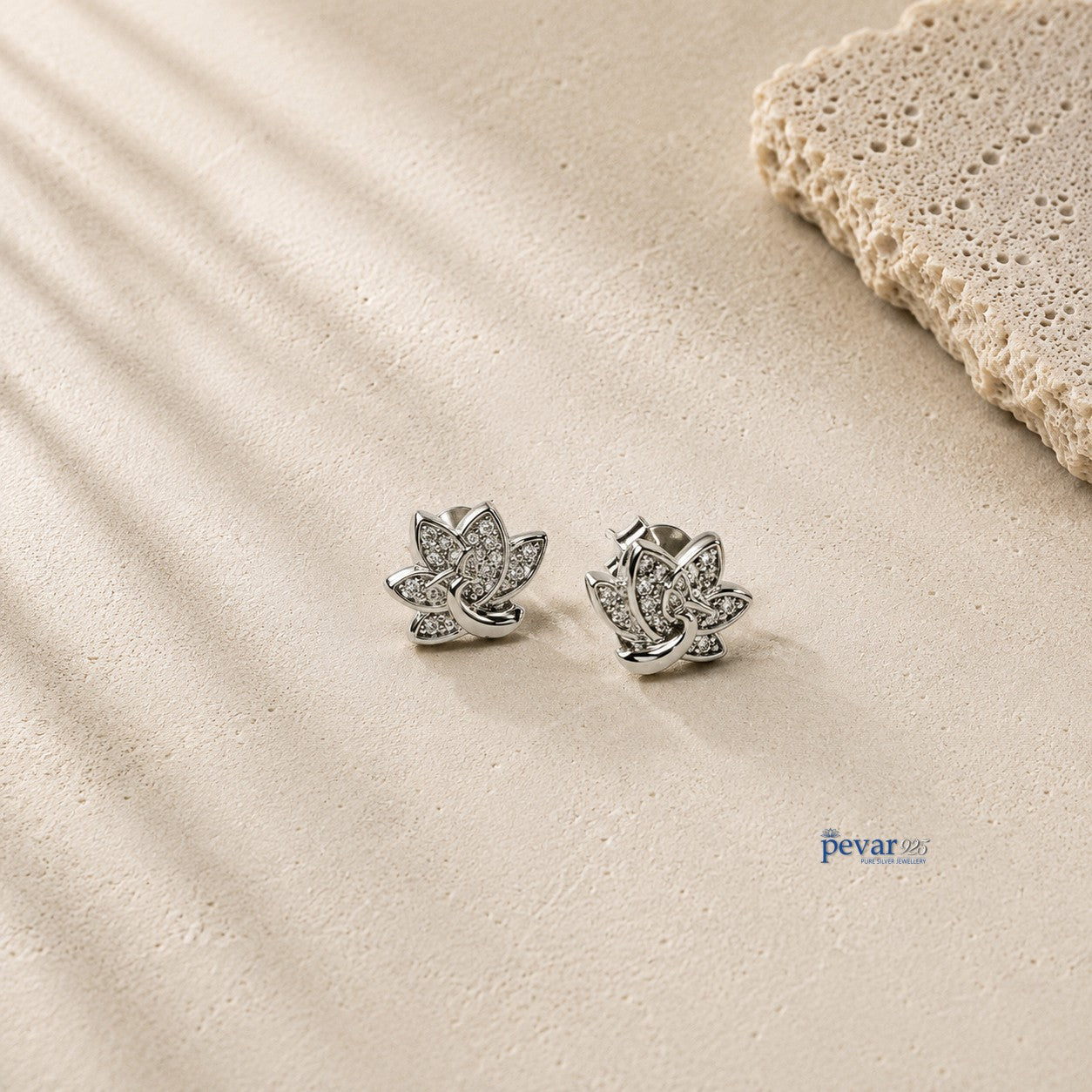 pevar925 sterling silver lotus stud earrings with rhodium plating and sparkling accents on a textured stone surface