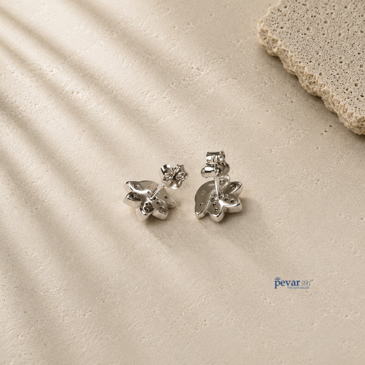 pevar925 sterling silver lotus stud earrings with rhodium plating and secure push-back clasps on a textured surface