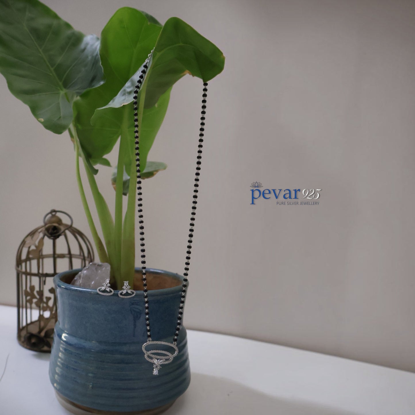 pevar925 sterling silver dual oval mangalsutra set with black beads and matching earrings on a blue ceramic pot