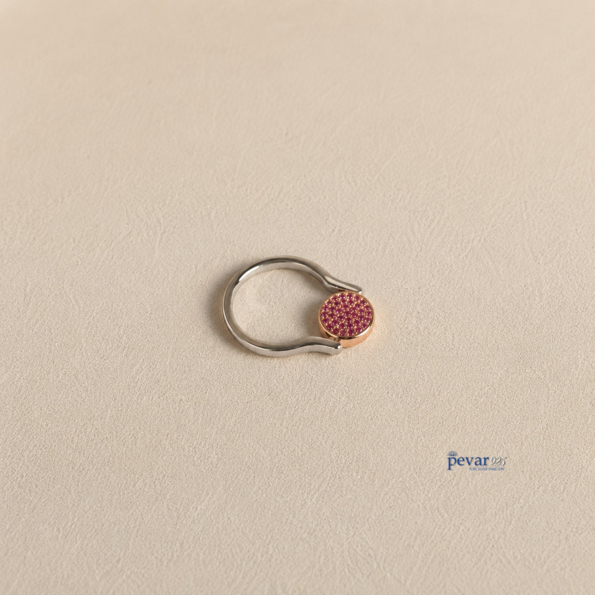 pevar925 sterling silver flip ring with a circular top featuring vibrant pink gemstones on a textured beige surface.