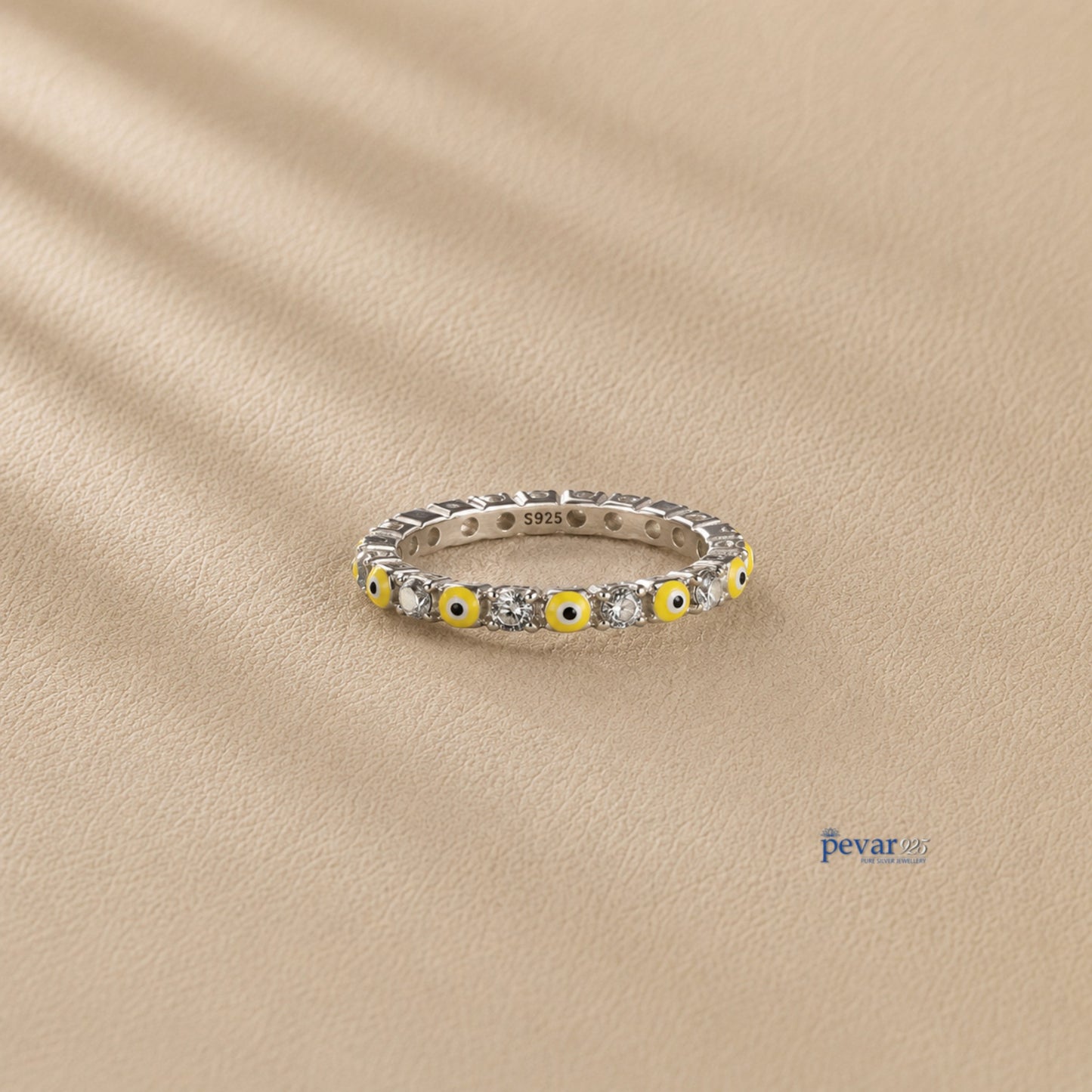 pevar925 sterling silver band ring featuring alternating yellow evil eye motifs and clear stones on a beige background